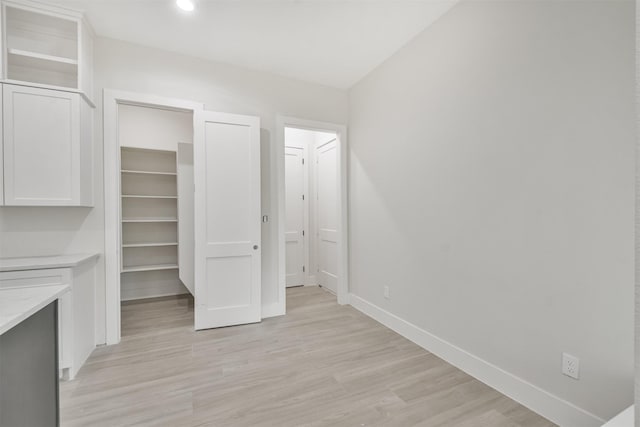 interior space with recessed lighting, baseboards, a closet, light wood finished floors, and a walk in closet