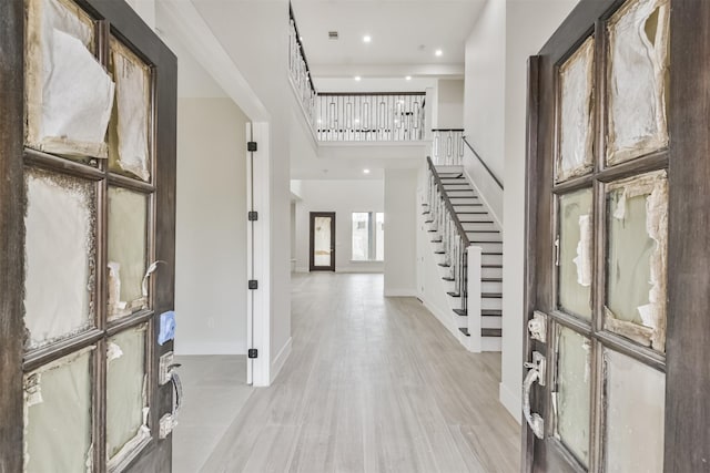 foyer entrance featuring recessed lighting, a high ceiling, baseboards, stairs, and light wood-style floors