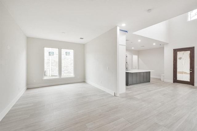 unfurnished living room featuring light wood-style floors, baseboards, a sink, and recessed lighting