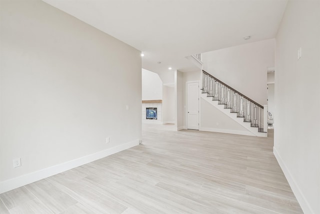 unfurnished living room featuring light wood-type flooring, stairway, and baseboards