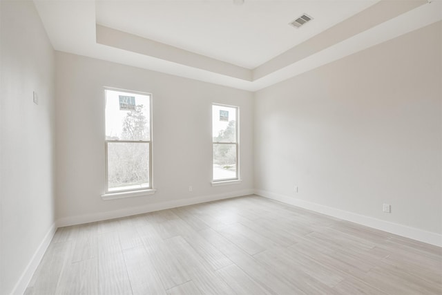 empty room with baseboards, visible vents, a raised ceiling, and light wood-style flooring