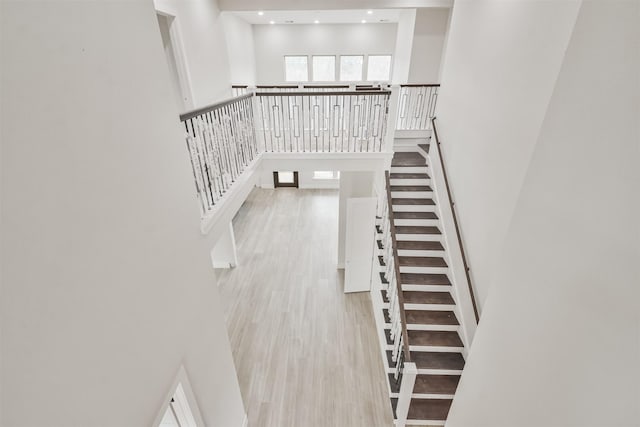 stairs with a towering ceiling, wood finished floors, and recessed lighting