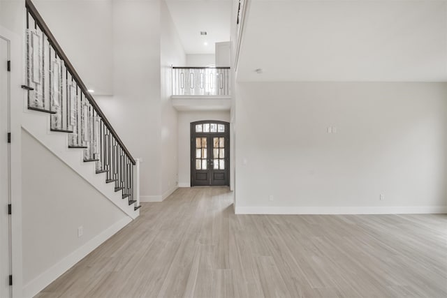 foyer entrance featuring light wood-type flooring, a towering ceiling, baseboards, and stairs