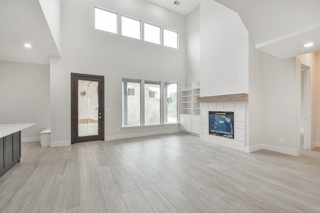 unfurnished living room with light wood-style floors, baseboards, and a tiled fireplace