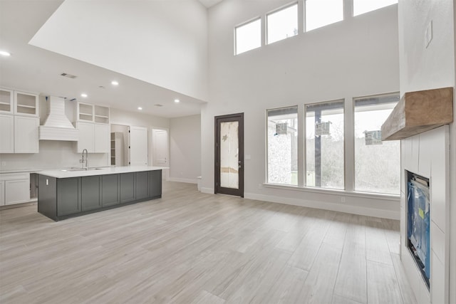 kitchen featuring light wood-type flooring, custom range hood, white cabinetry, and a center island with sink