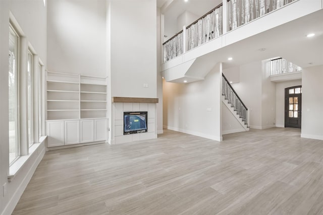 unfurnished living room with a towering ceiling, wood finished floors, a tile fireplace, baseboards, and stairs