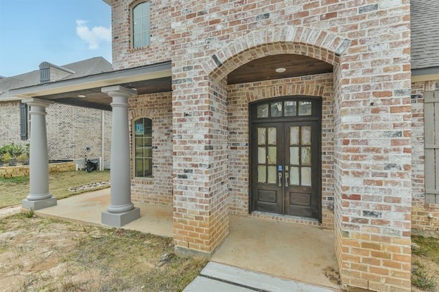 doorway to property featuring brick siding, roof with shingles, and french doors