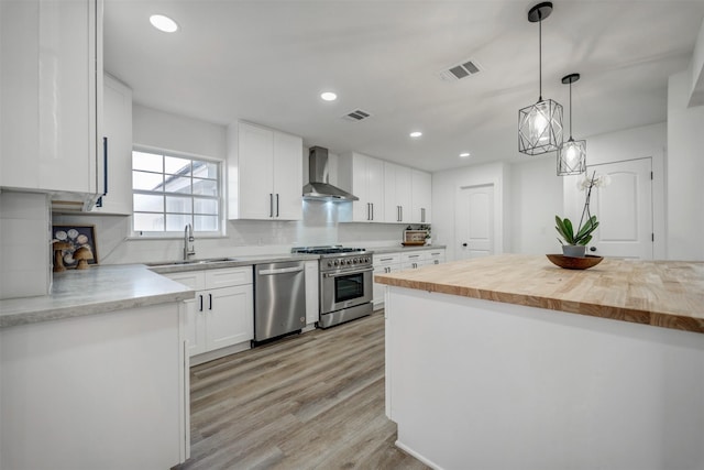 kitchen featuring stainless steel appliances, wall chimney exhaust hood, a sink, and visible vents