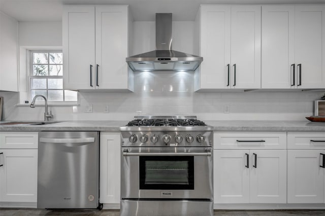 kitchen with stainless steel appliances, wall chimney range hood, a sink, and white cabinetry