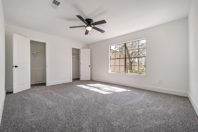 unfurnished bedroom featuring carpet, multiple closets, visible vents, ceiling fan, and baseboards