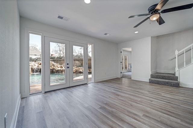 unfurnished living room with baseboards, visible vents, stairway, wood finished floors, and french doors