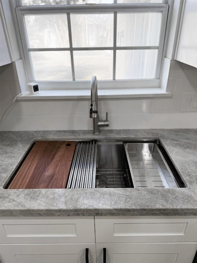 room details featuring light stone counters, a sink, and white cabinets