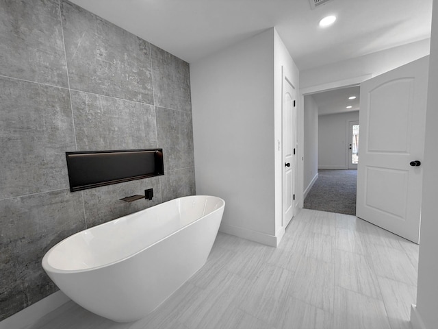 full bath with baseboards, tile walls, a freestanding bath, and recessed lighting