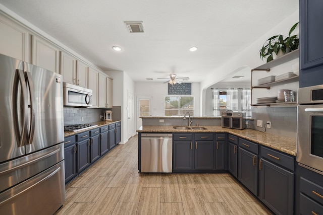 kitchen featuring stainless steel appliances, a peninsula, a sink, visible vents, and tasteful backsplash