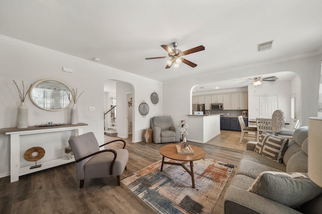 living room featuring light wood finished floors, visible vents, arched walkways, a ceiling fan, and stairs