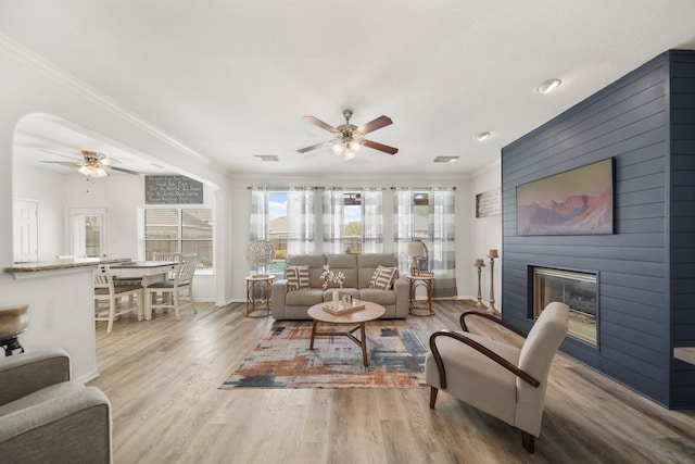 living room featuring ceiling fan, a fireplace, ornamental molding, and wood finished floors