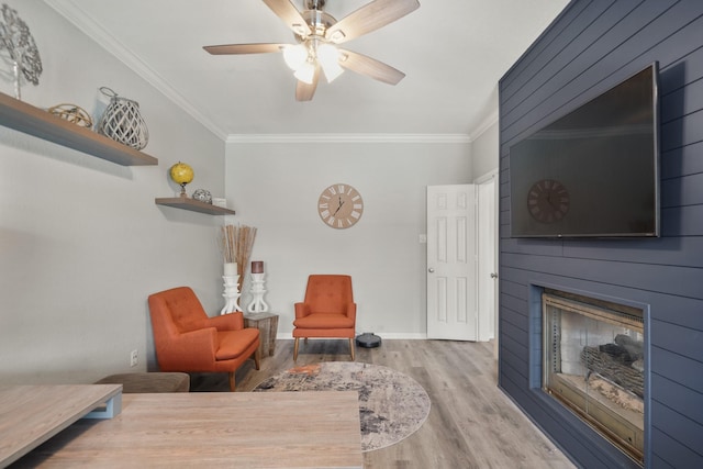 sitting room featuring a large fireplace, ornamental molding, wood finished floors, and baseboards