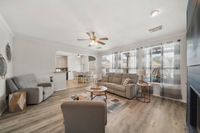 living area with arched walkways, visible vents, ornamental molding, light wood-type flooring, and baseboards