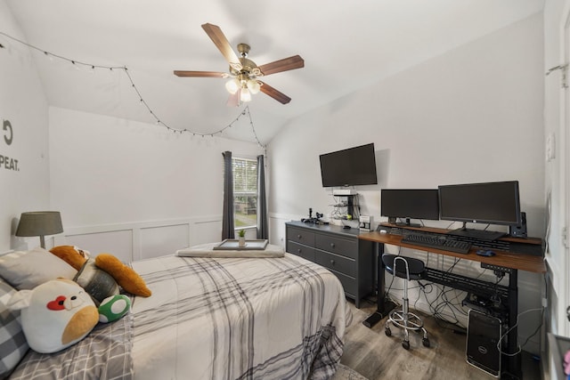 bedroom featuring wainscoting, ceiling fan, wood finished floors, vaulted ceiling, and a decorative wall