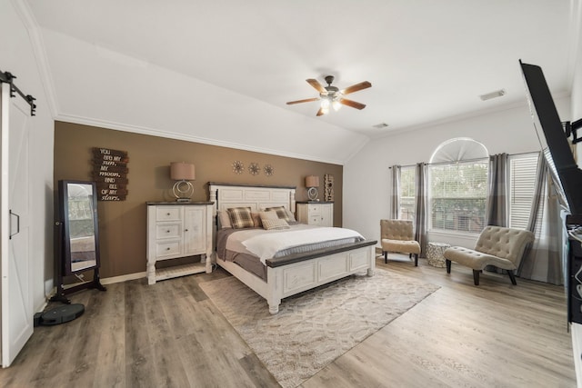 bedroom featuring light wood-type flooring, lofted ceiling, visible vents, and a barn door