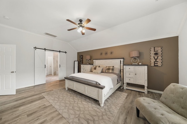 bedroom with a barn door, visible vents, lofted ceiling, crown molding, and light wood-style floors