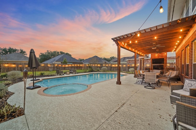 pool at dusk with a ceiling fan, a patio area, a fenced backyard, and a fireplace