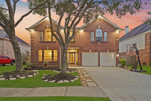 traditional-style home featuring brick siding, a lawn, an attached garage, fence, and driveway