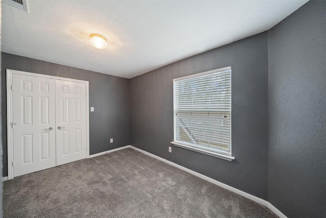 unfurnished bedroom featuring a closet, visible vents, dark carpet, and baseboards