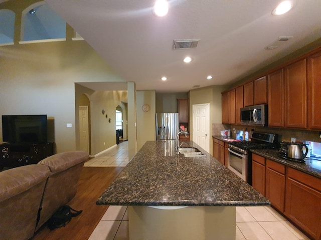 kitchen featuring arched walkways, a sink, open floor plan, appliances with stainless steel finishes, and brown cabinets