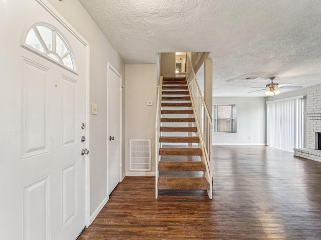 entryway featuring a brick fireplace, visible vents, stairway, and wood finished floors