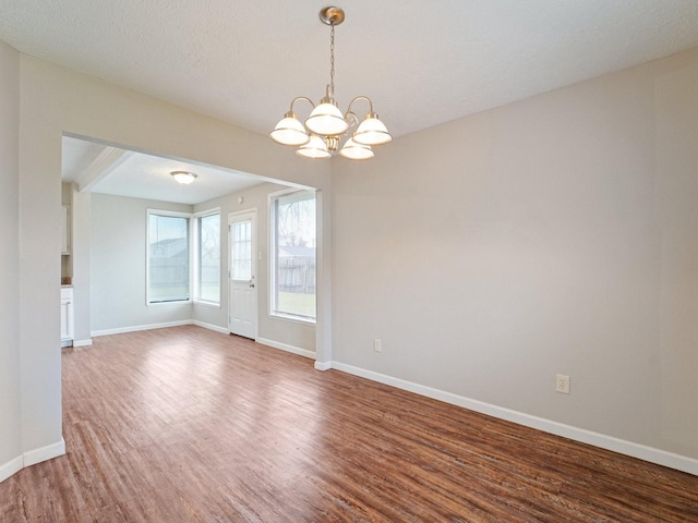 empty room with a chandelier, a textured ceiling, baseboards, and wood finished floors