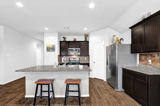 kitchen featuring appliances with stainless steel finishes, a sink, a kitchen bar, and dark wood-style floors