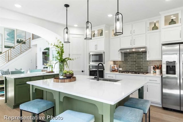 kitchen featuring a kitchen breakfast bar, light countertops, stainless steel appliances, under cabinet range hood, and a sink