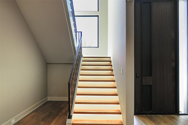 stairway with baseboards, elevator, wood finished floors, and vaulted ceiling