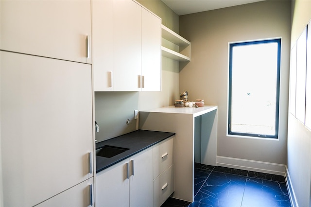 kitchen featuring marble finish floor, a sink, open shelves, white cabinetry, and baseboards