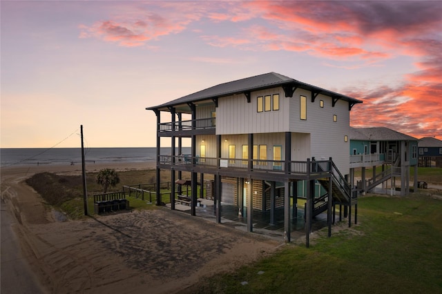 back of property at dusk with a yard, driveway, a balcony, and stairs