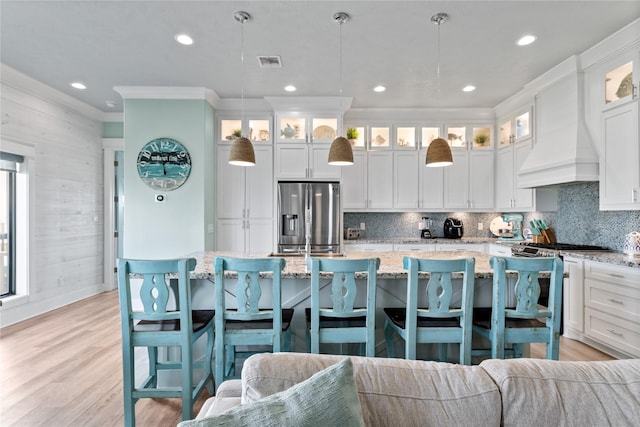 kitchen with stainless steel appliances, premium range hood, light wood-style floors, tasteful backsplash, and a center island with sink