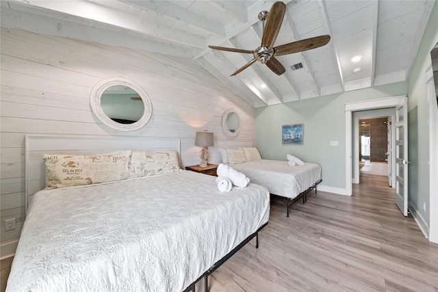 bedroom with wooden walls, baseboards, visible vents, wood finished floors, and vaulted ceiling with beams