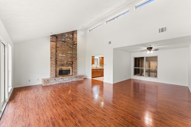 unfurnished living room with a ceiling fan, visible vents, a fireplace, and wood finished floors