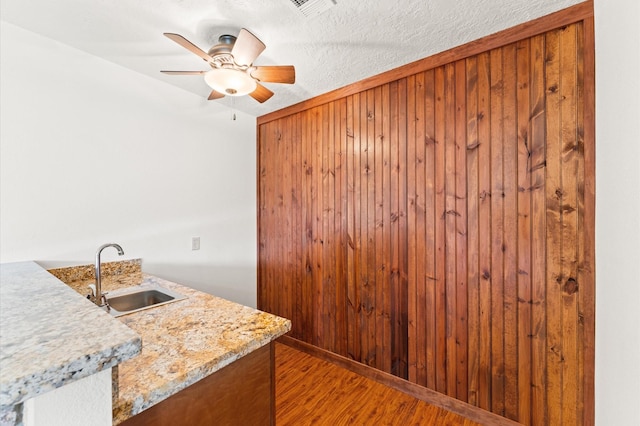 kitchen featuring light wood finished floors, ceiling fan, a sink, wooden walls, and a textured ceiling