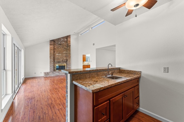 kitchen featuring lofted ceiling, a brick fireplace, a sink, and wood finished floors