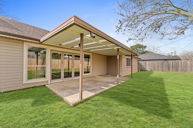 back of house with brick siding, a patio, a shingled roof, a lawn, and fence