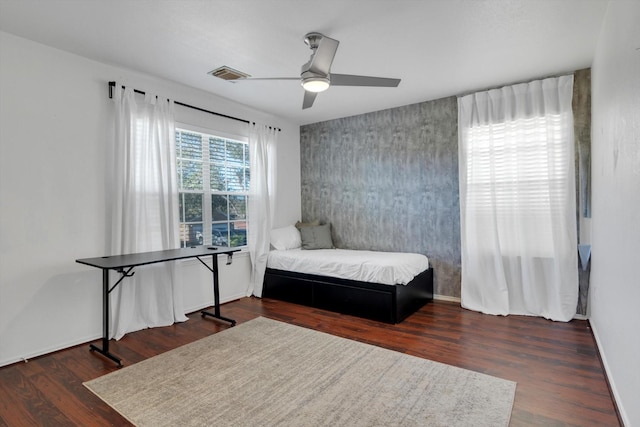 bedroom with an accent wall, wood finished floors, a ceiling fan, visible vents, and baseboards