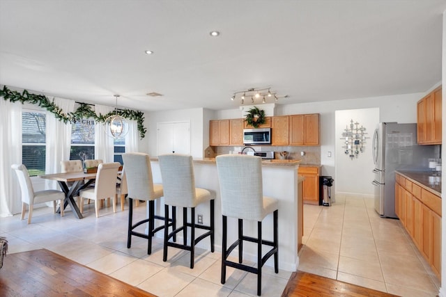 kitchen featuring light tile patterned floors, an island with sink, stainless steel microwave, a breakfast bar, and backsplash