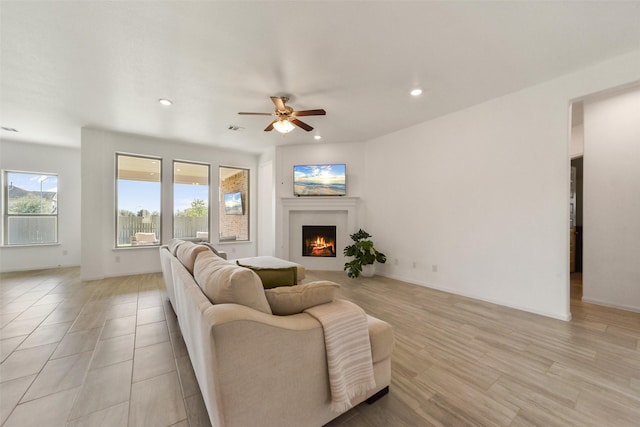 living room with a warm lit fireplace, recessed lighting, a ceiling fan, light wood-style floors, and baseboards