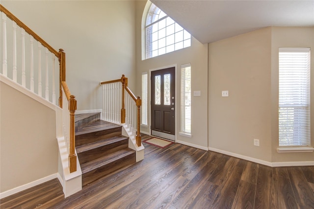 foyer with a towering ceiling, dark wood-style floors, stairs, and baseboards