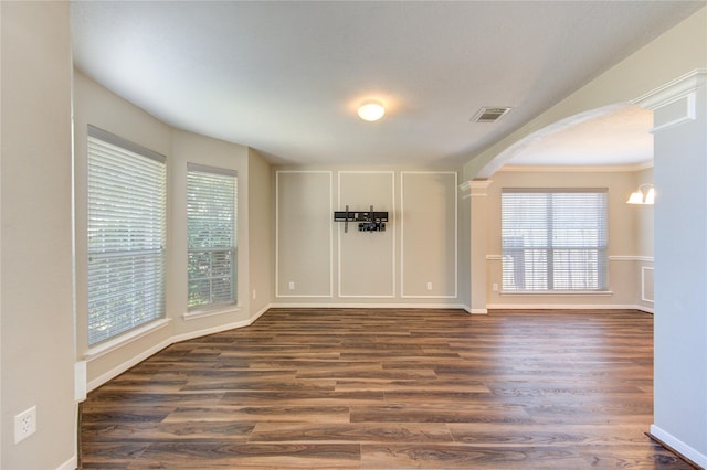 unfurnished room featuring arched walkways, dark wood finished floors, and visible vents