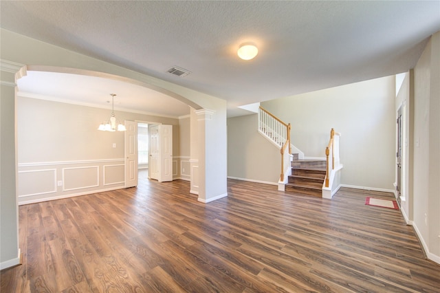 empty room featuring visible vents, arched walkways, dark wood-style flooring, stairs, and a textured ceiling