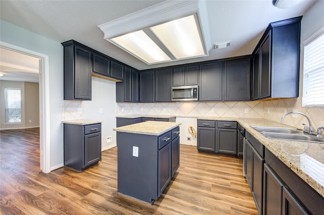 kitchen with light wood finished floors, stainless steel microwave, a sink, and a healthy amount of sunlight