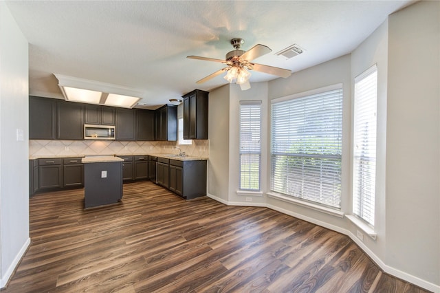 kitchen featuring visible vents, decorative backsplash, dark wood finished floors, stainless steel microwave, and a sink